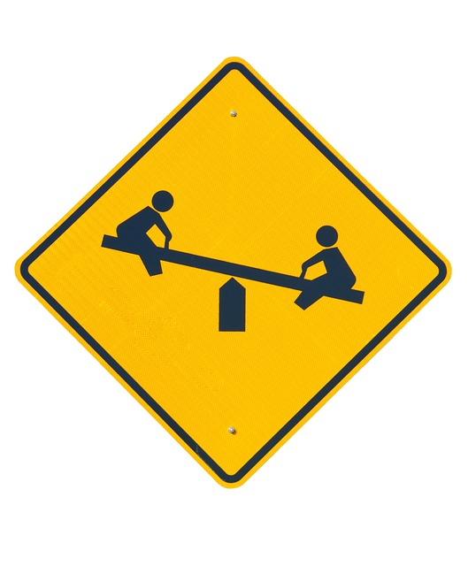 A yellow road sign of two children on a see-saw.
