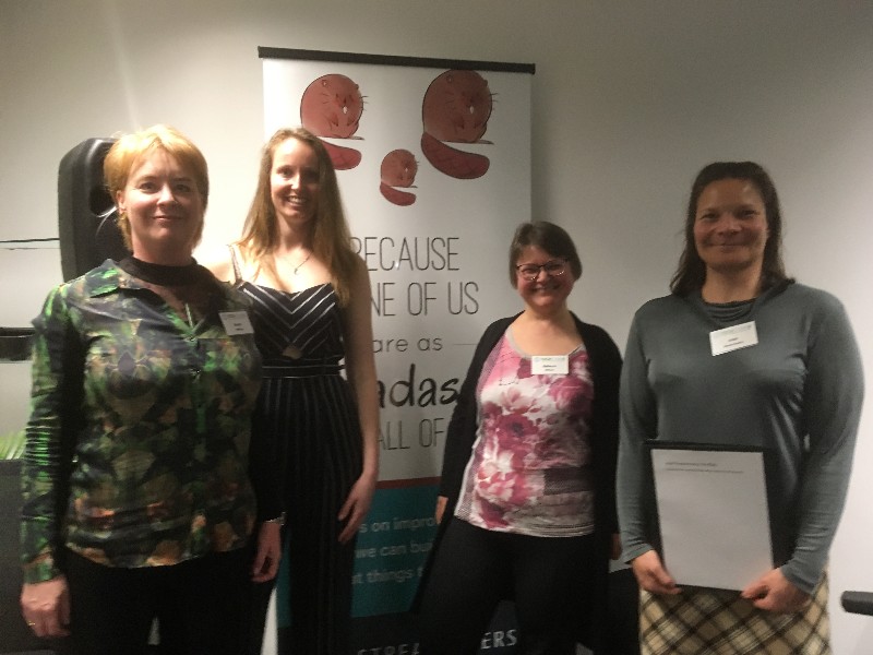 Left to right: Emma Harding, Eve Hoets, Rebecca Office and Joan Nanartowicz. They are standing in front of a banner that says 