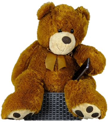 A smiling brown teddy bear is holding a mobile phone with its left paw. The phone is balanced on its left knee.